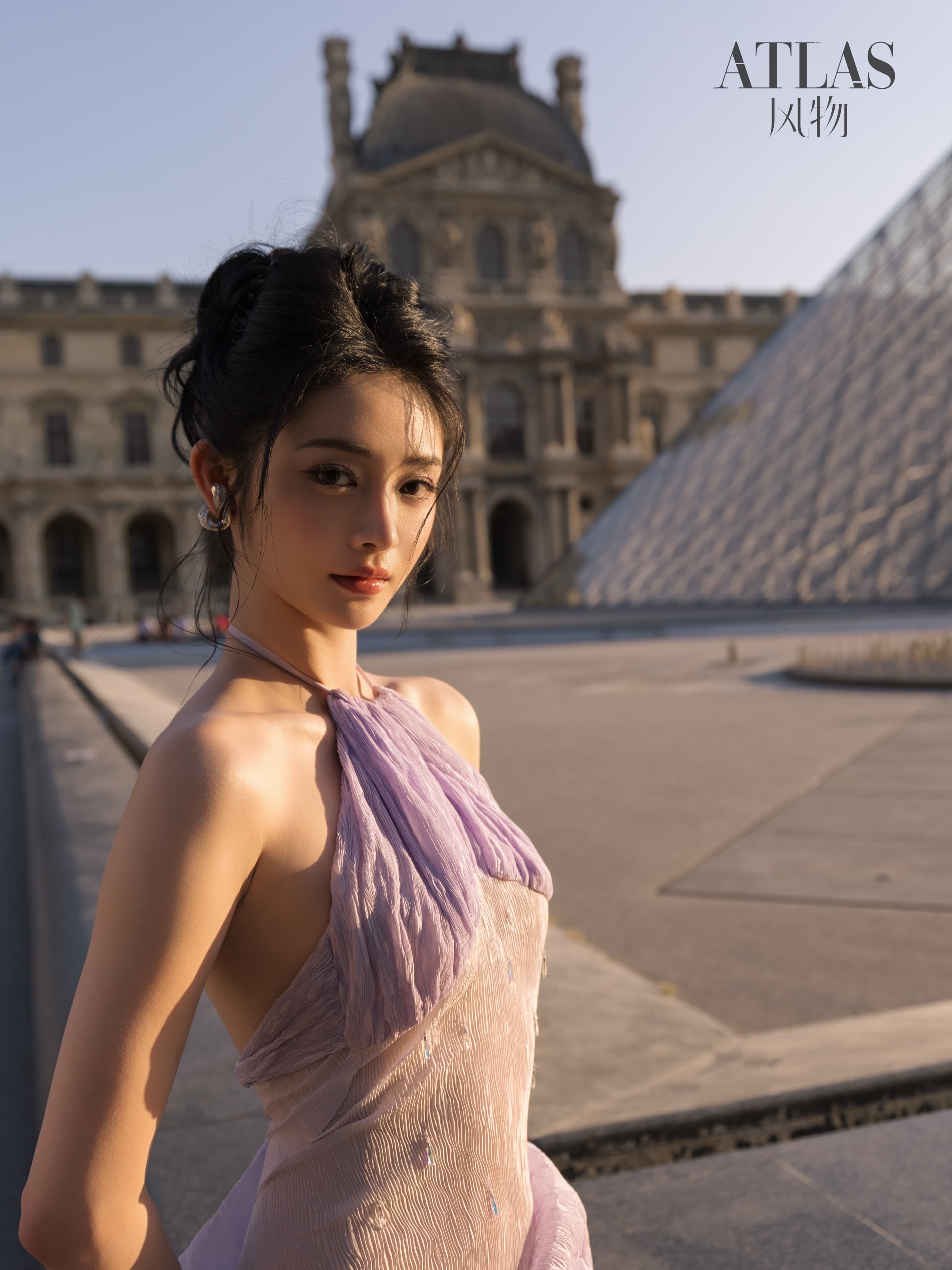 Zhou Jieqiong before the Louvre pyramid in warm evening light.