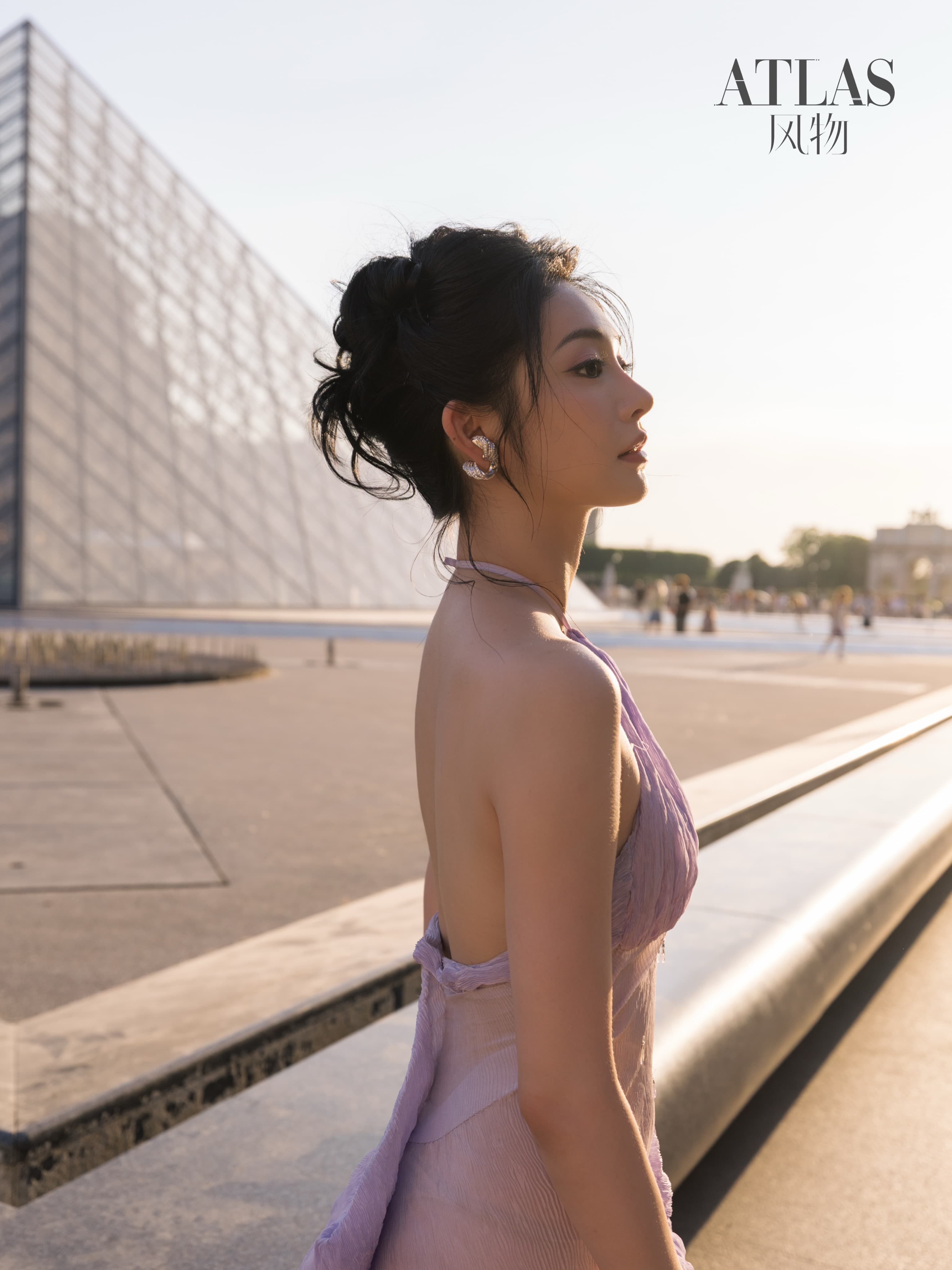 Zhou Jieqiong in profile beside the Louvre pyramid and reflecting pool.