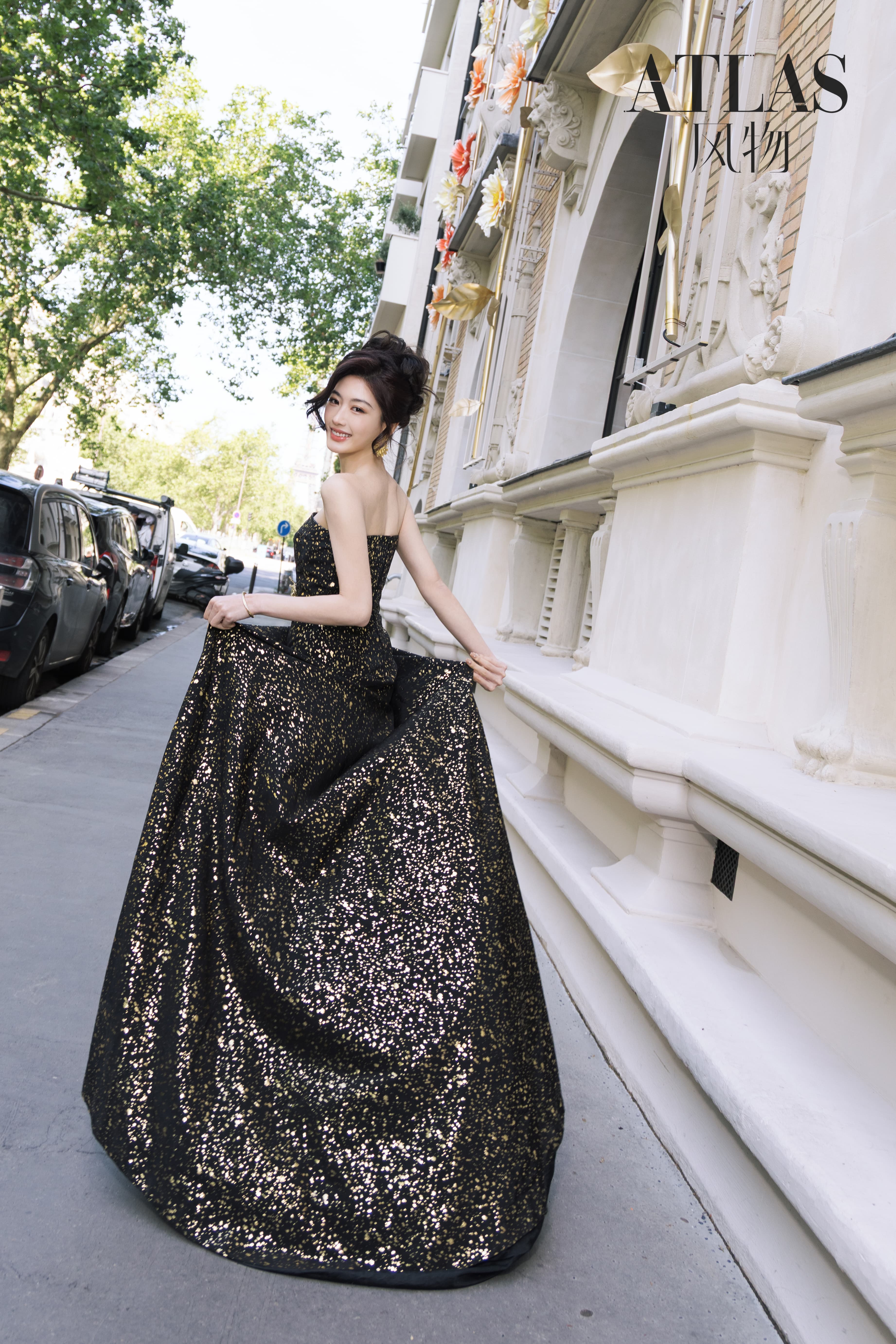 Sun Leyan holding the volume of a black-and-gold dress on a Paris street.