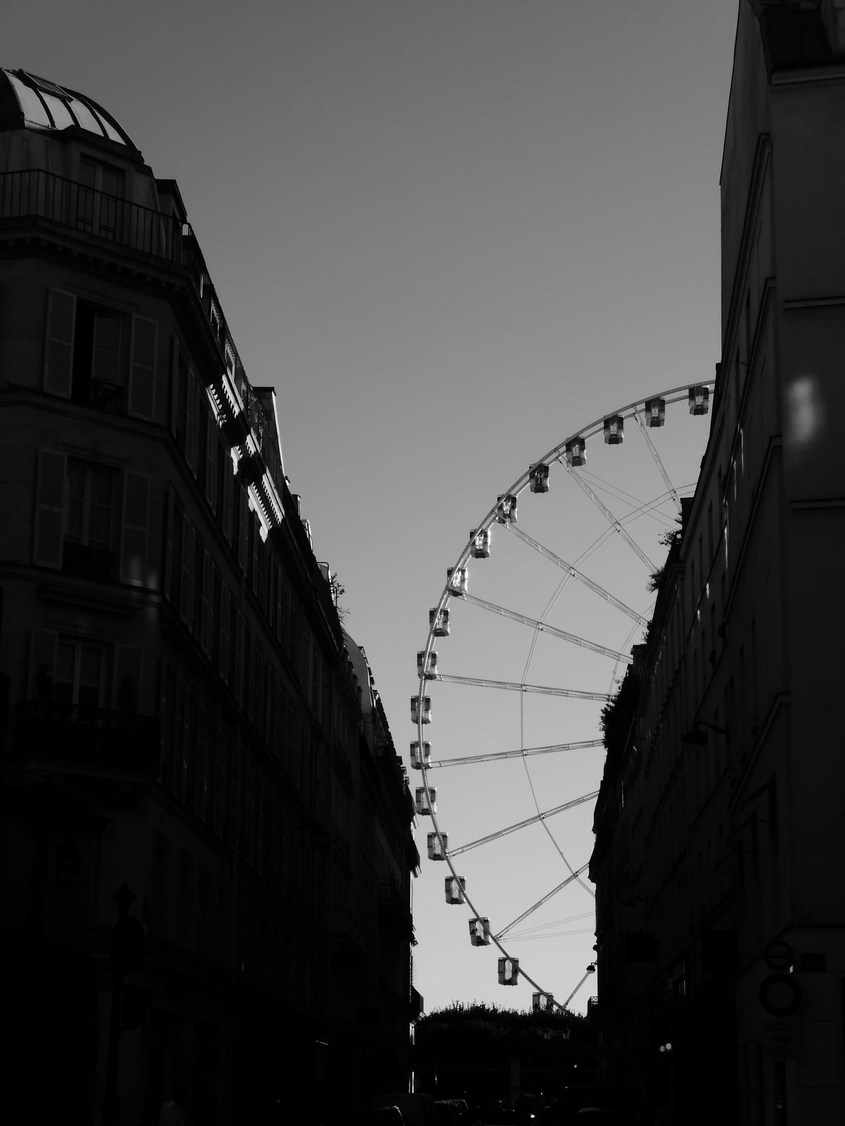 A ferris wheel glimpsed between dark Paris buildings.